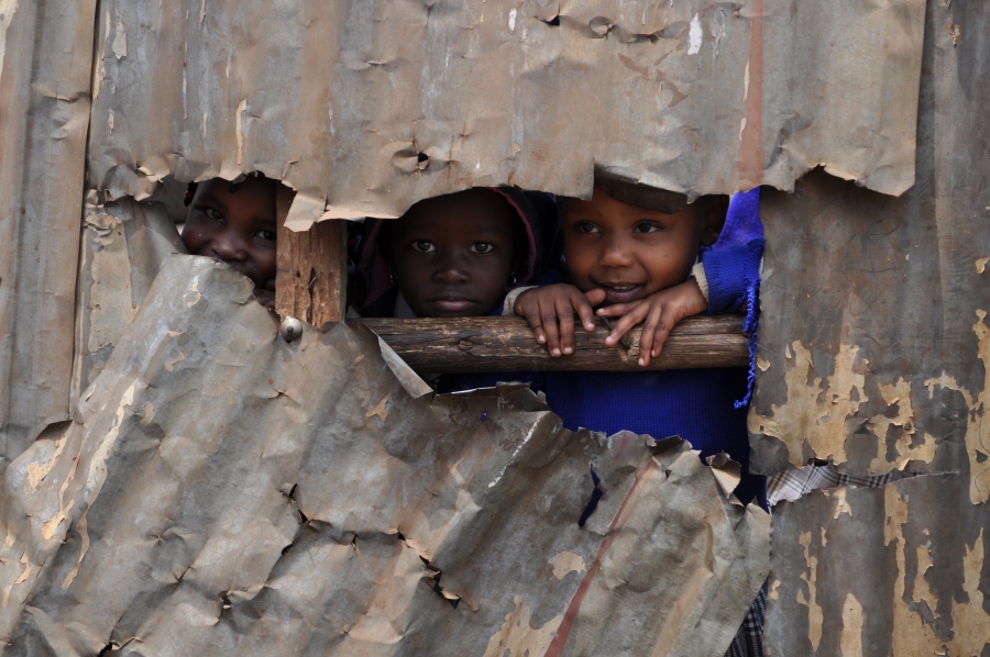Kenyan children peek through a broken tin wall